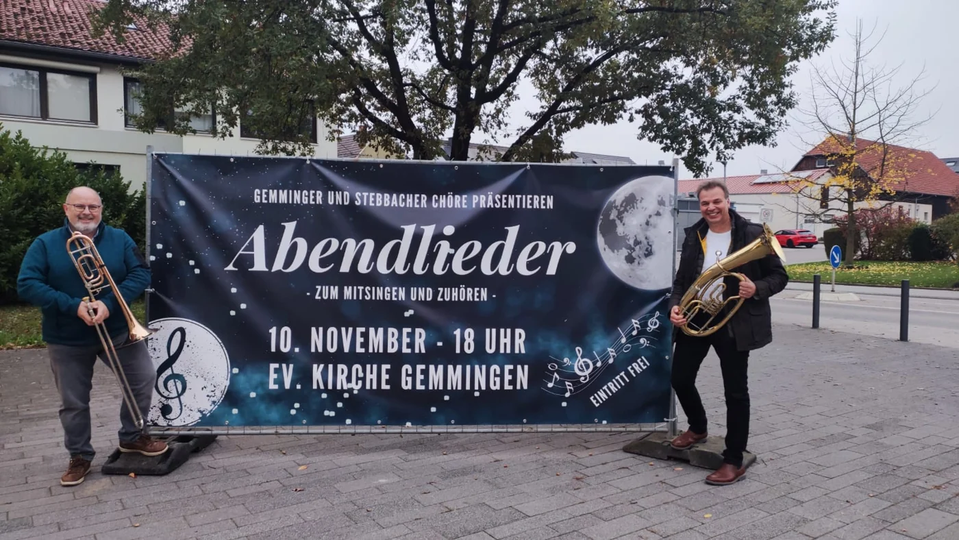 Musiker mit einem Veranstaltungsbanner für das Abendliedersingen 2024